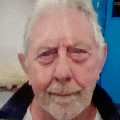 Elderly man with grey hair and a faint smile, wearing a dark jacket.