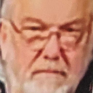 An elderly man with glasses, a beard, and a serious expression.